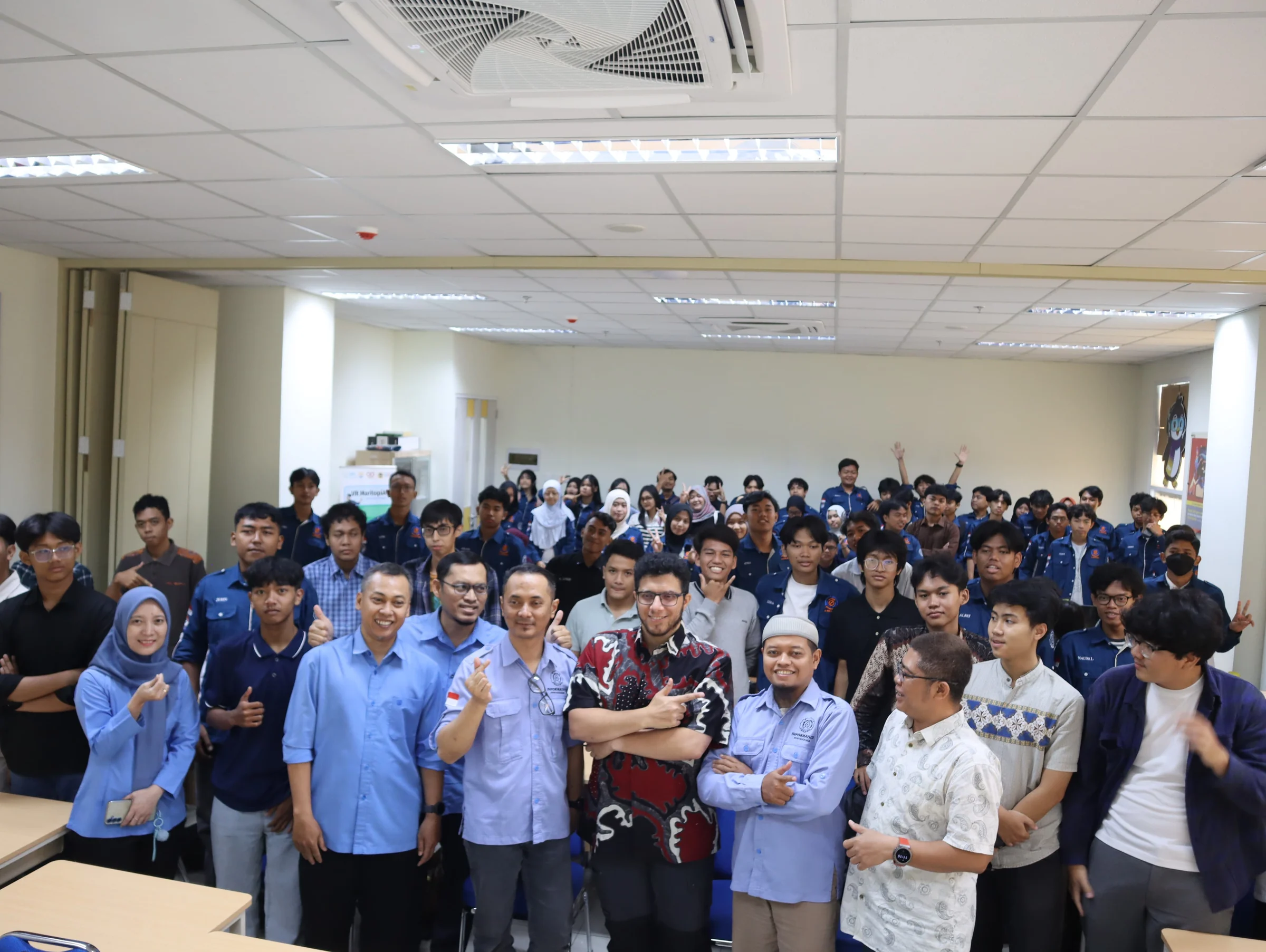 Group photo after the lecture: Omer Kara, arms crossed, in the middle of the students and staff, many of them making a V sign