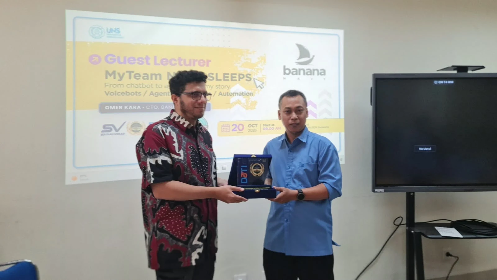 Omer Kara receives a souvenir plaque in front of the poster of his lecture, My team never sleeps